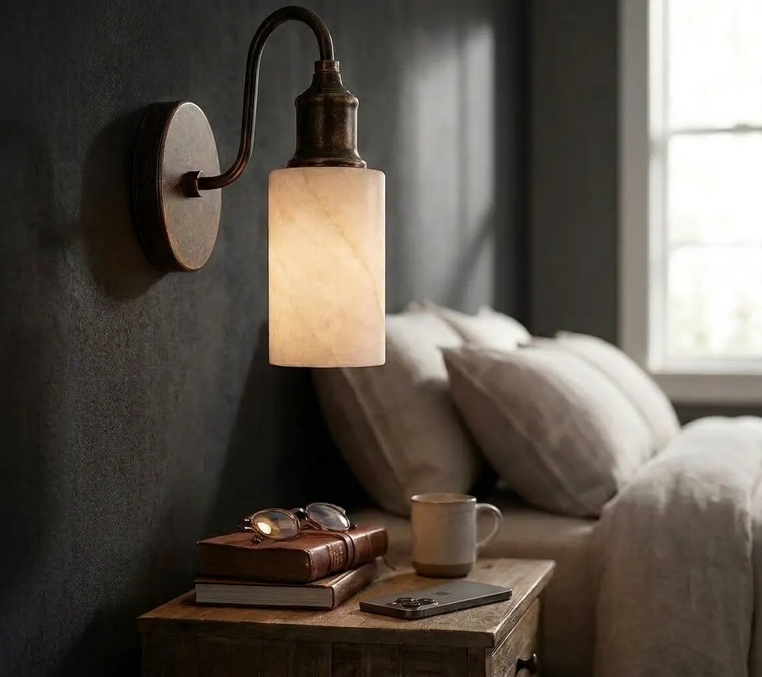 Gooseneck alabaster cylinder wall sconce beside a bedroom nightstand with books and a coffee cup