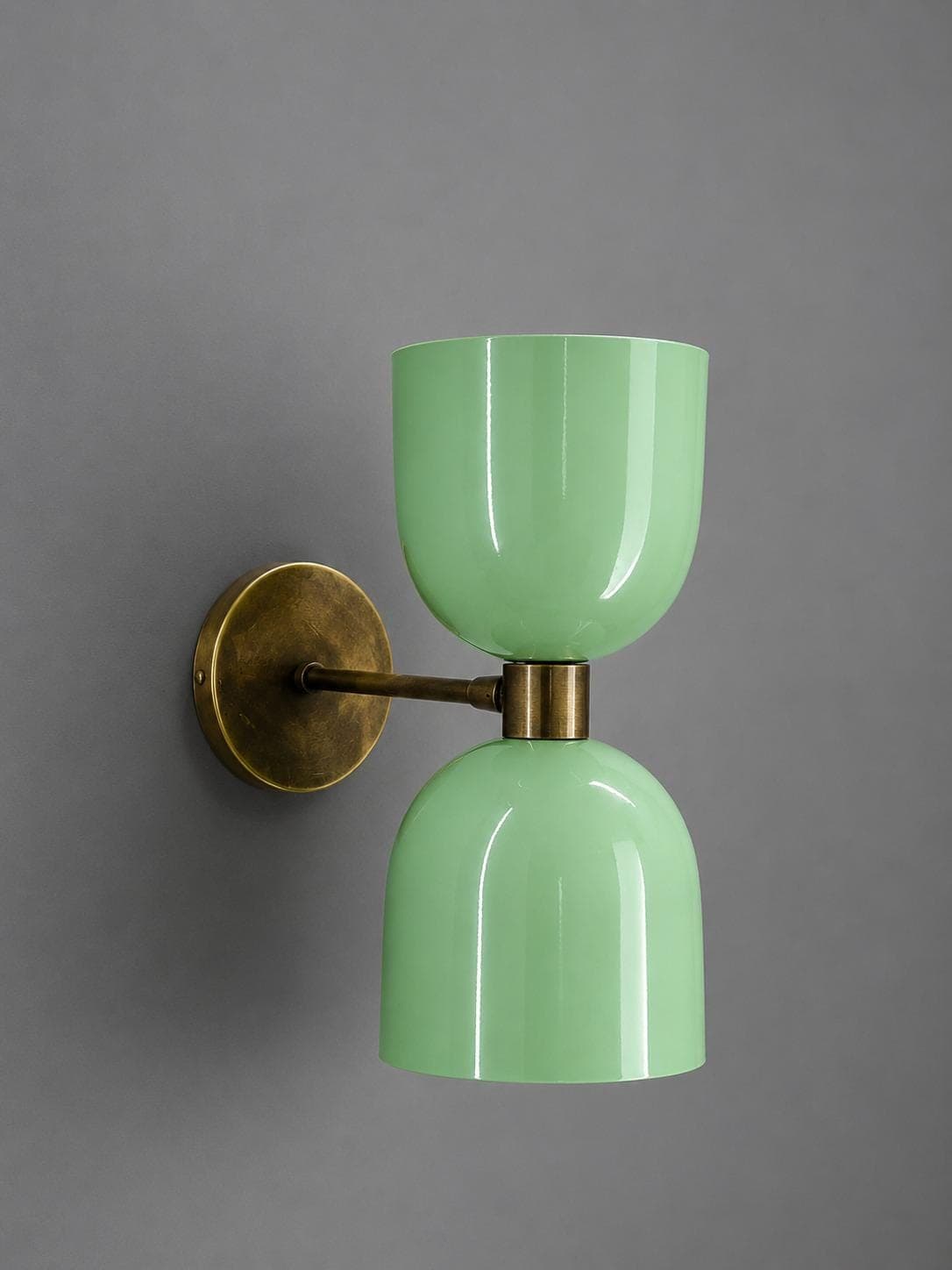 Mint green double-shade brass wall sconce with one cup facing up and one facing down on an aged brass arm and round backplate