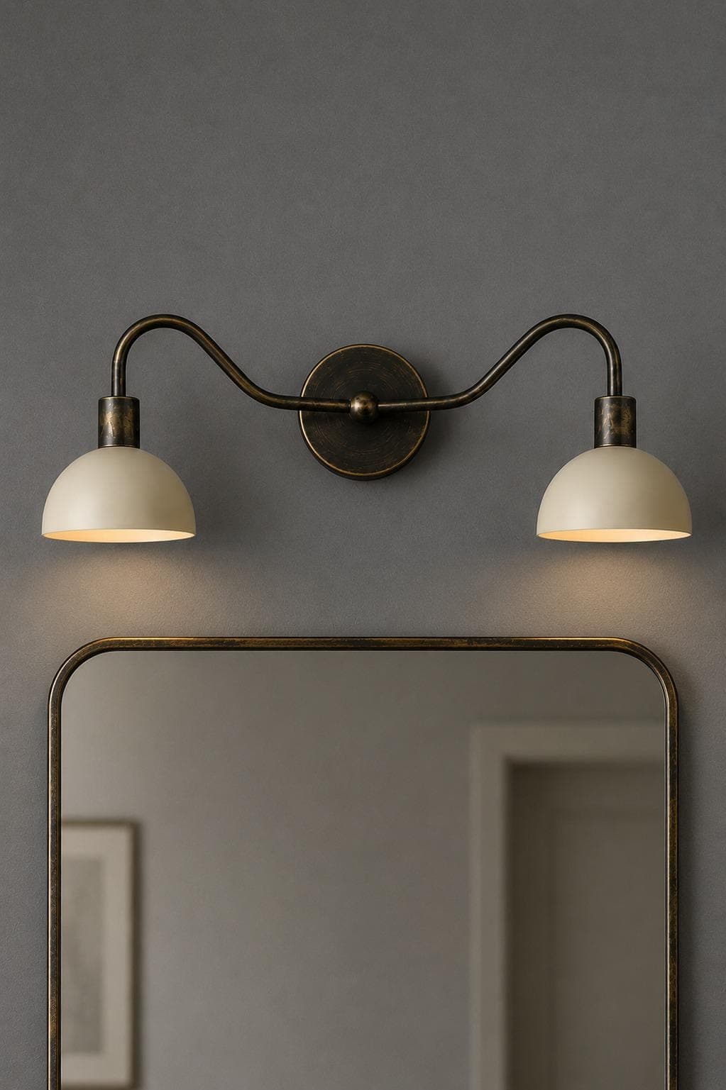 Two-light wall sconce with swan-neck antique black brass arms and cream dome shades lit above a brass-framed mirror