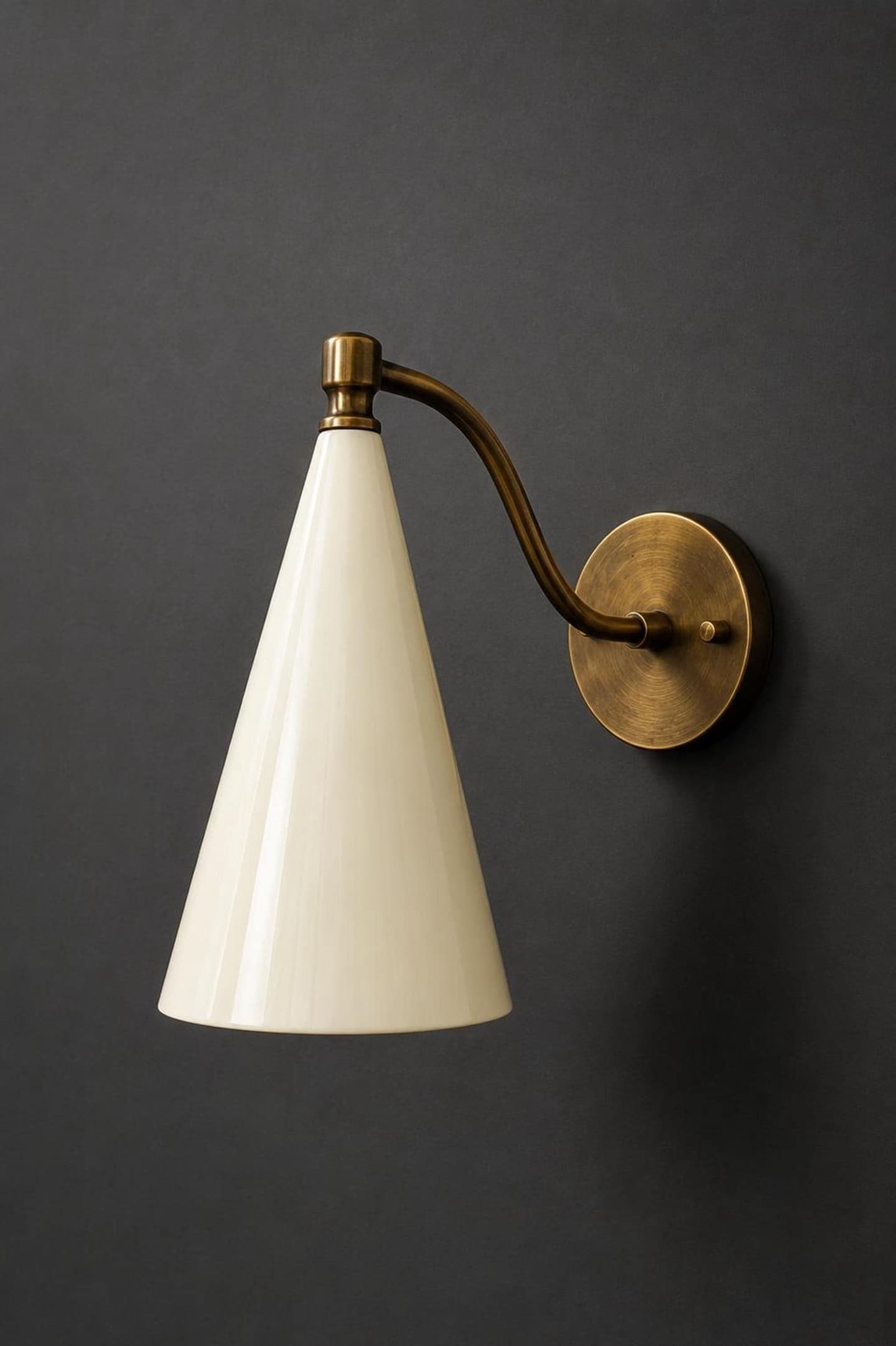 Solid brass wall sconce with a curved arm and a tapered glossy cream cone shade on a round brass backplate