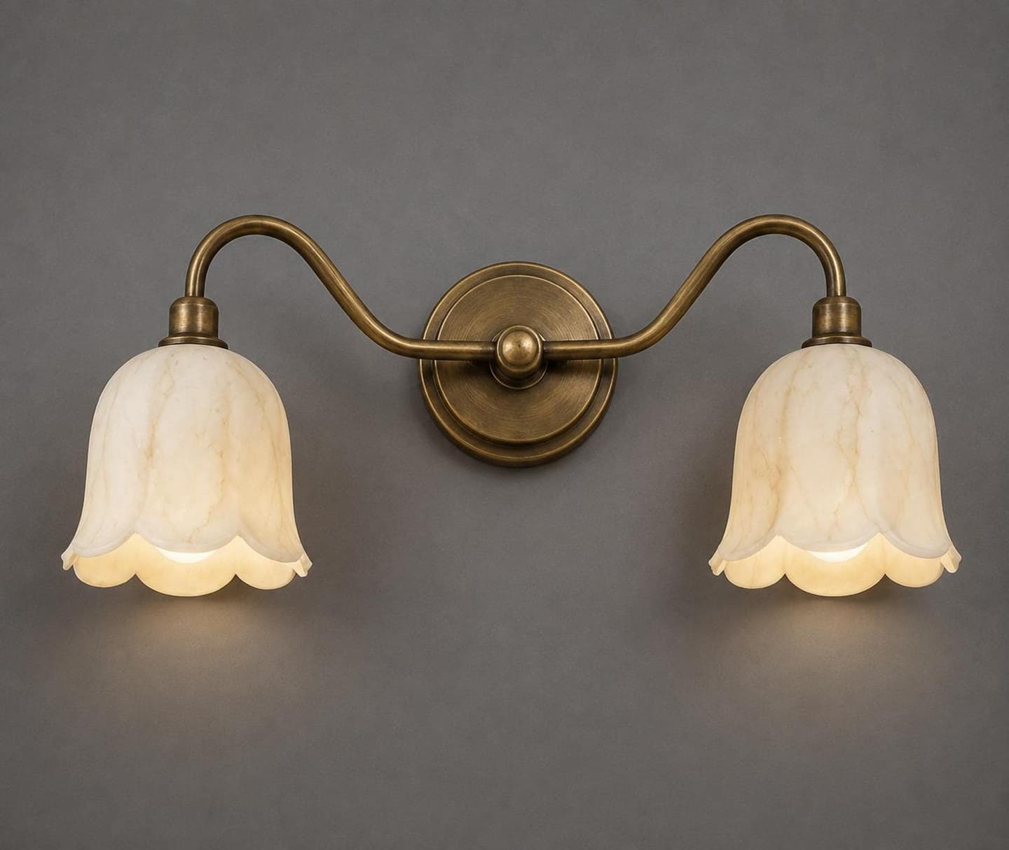 Two-light wall sconce with veined alabaster tulip shades and scalloped edges on curved antique brass arms and a round backplate