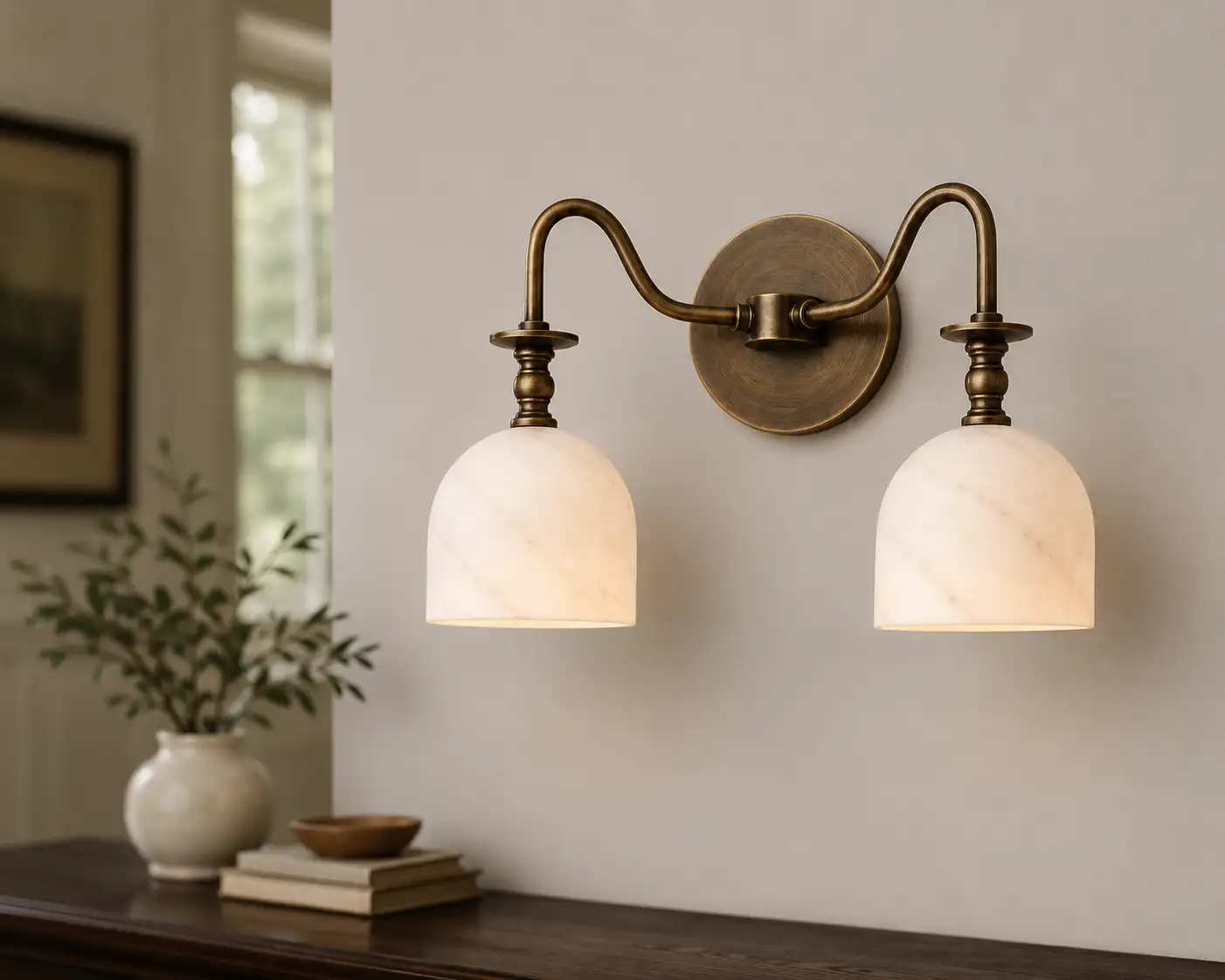 Twin-arm alabaster bell-shade vanity sconce above a console table with a vase and bowl
