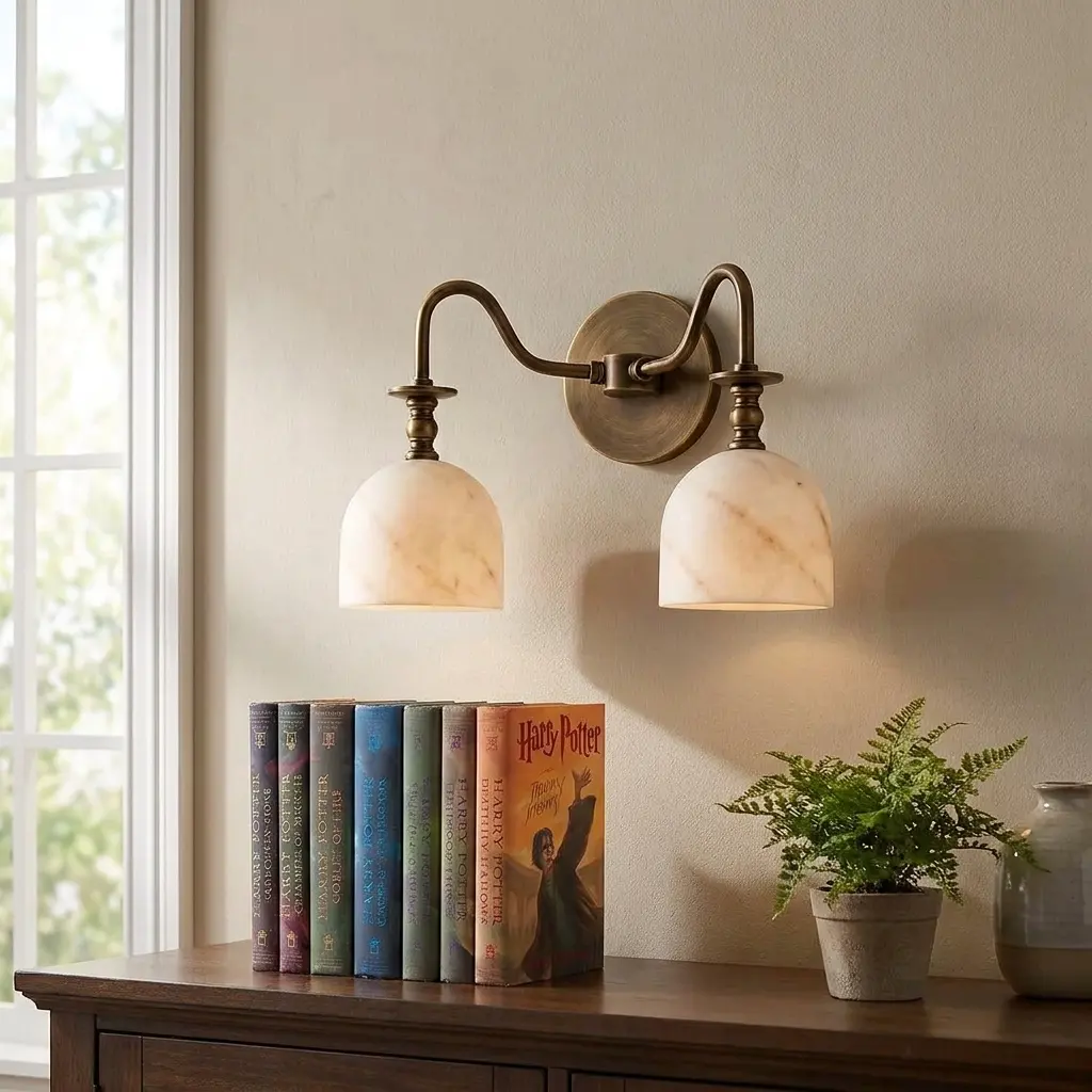Twin-arm alabaster bell-shade wall sconce above a stack of books and a potted fern