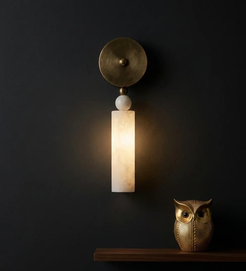 Alabaster ball-and-cylinder pillar wall sconce above a shelf with a brass owl figurine