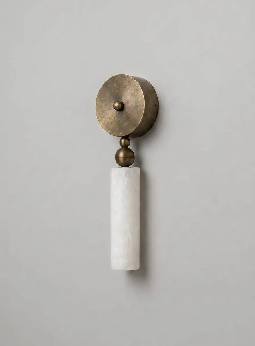 Alabaster ball-and-cylinder pillar wall sconce in aged brass finish on a plain neutral wall